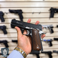 Pistola traumática Kuzey 911 SX bitono en mano, corredera negra con detalles plateados cromados y cachas de madera oscura cuadriculada, estilo clásico 1911, en tienda PaD Guns